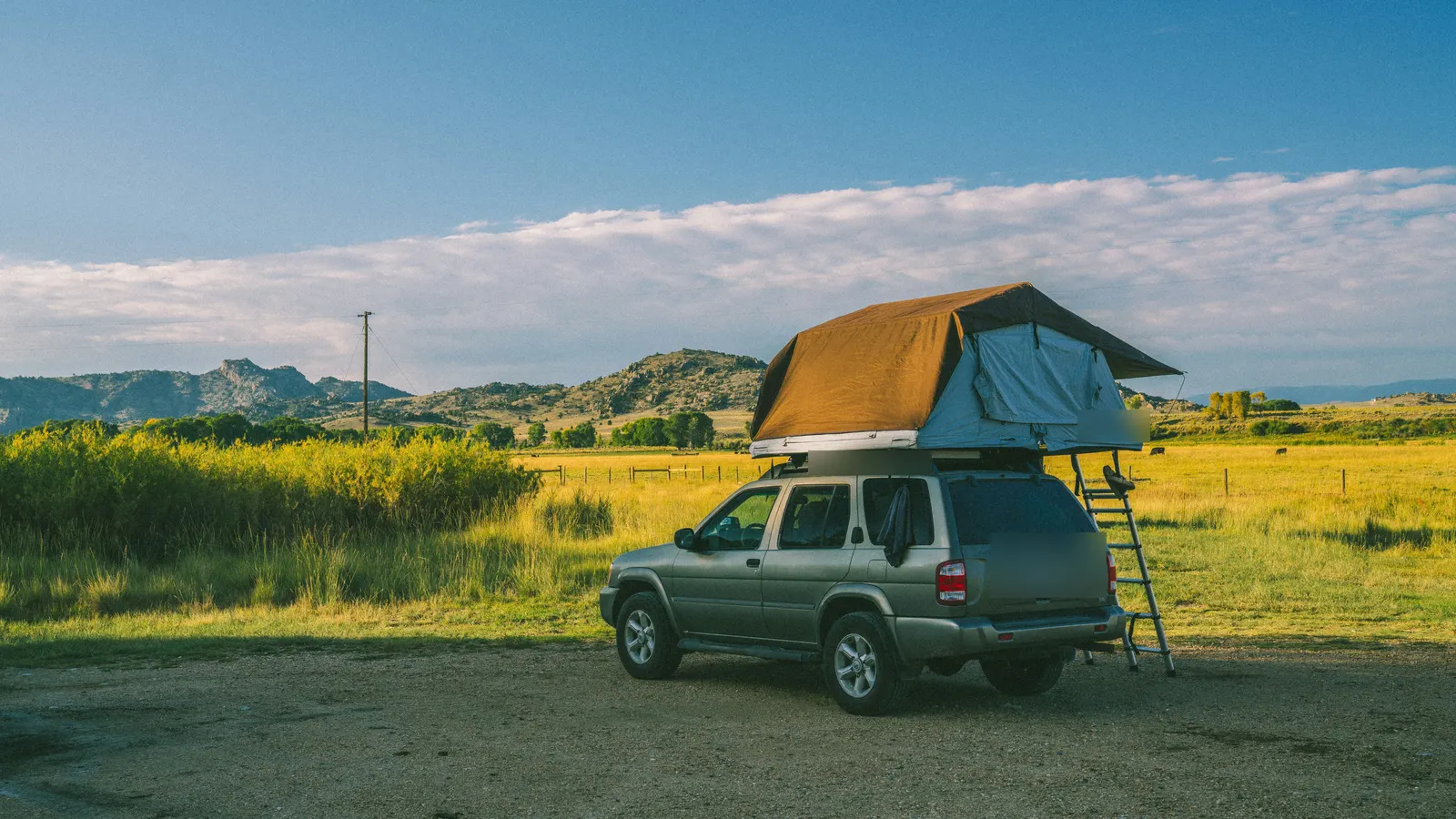 An SUV parked by a field with its roof tent open and the ladder down