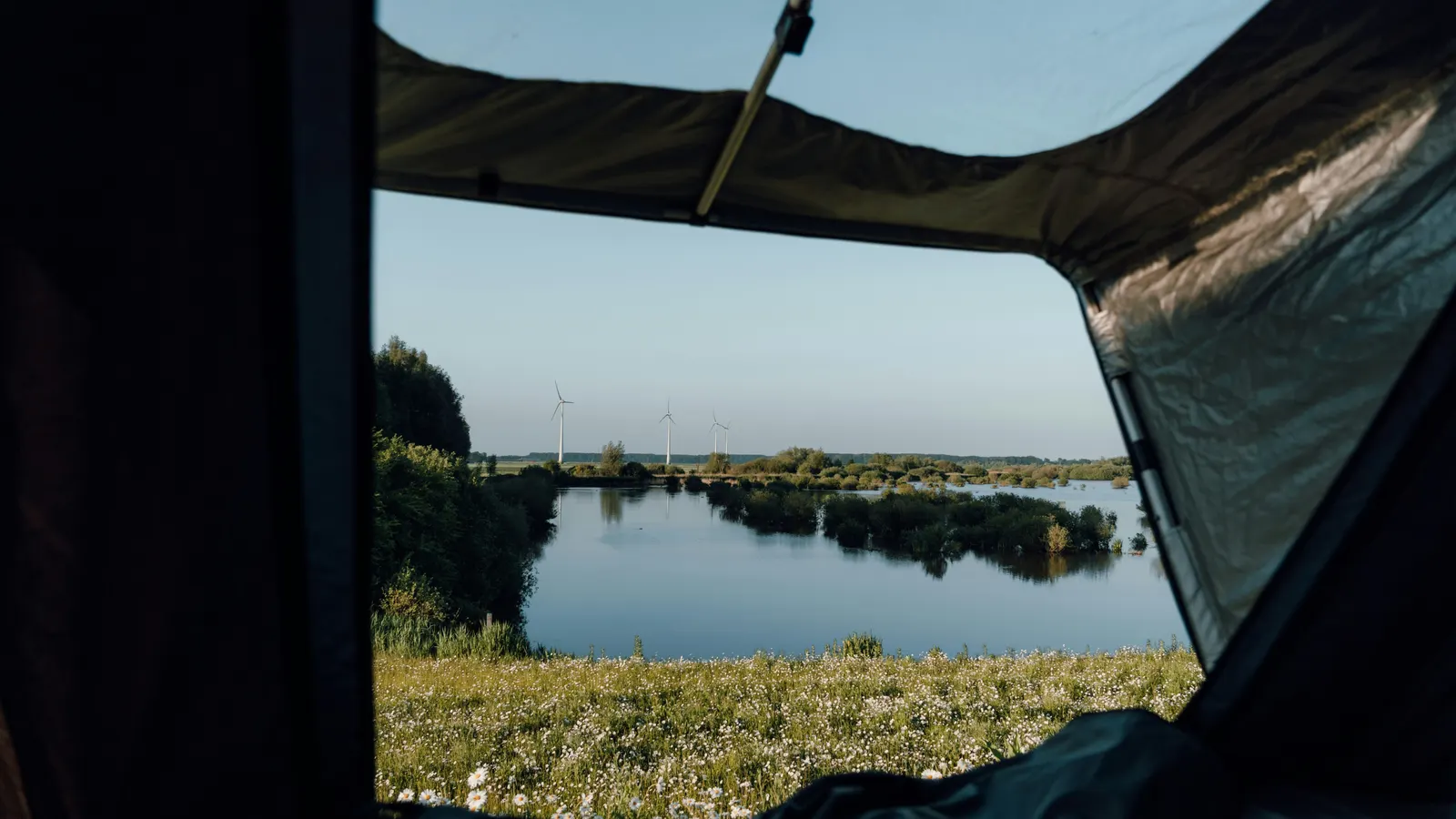 The view out of an open roof tent across a meadow to a still lake